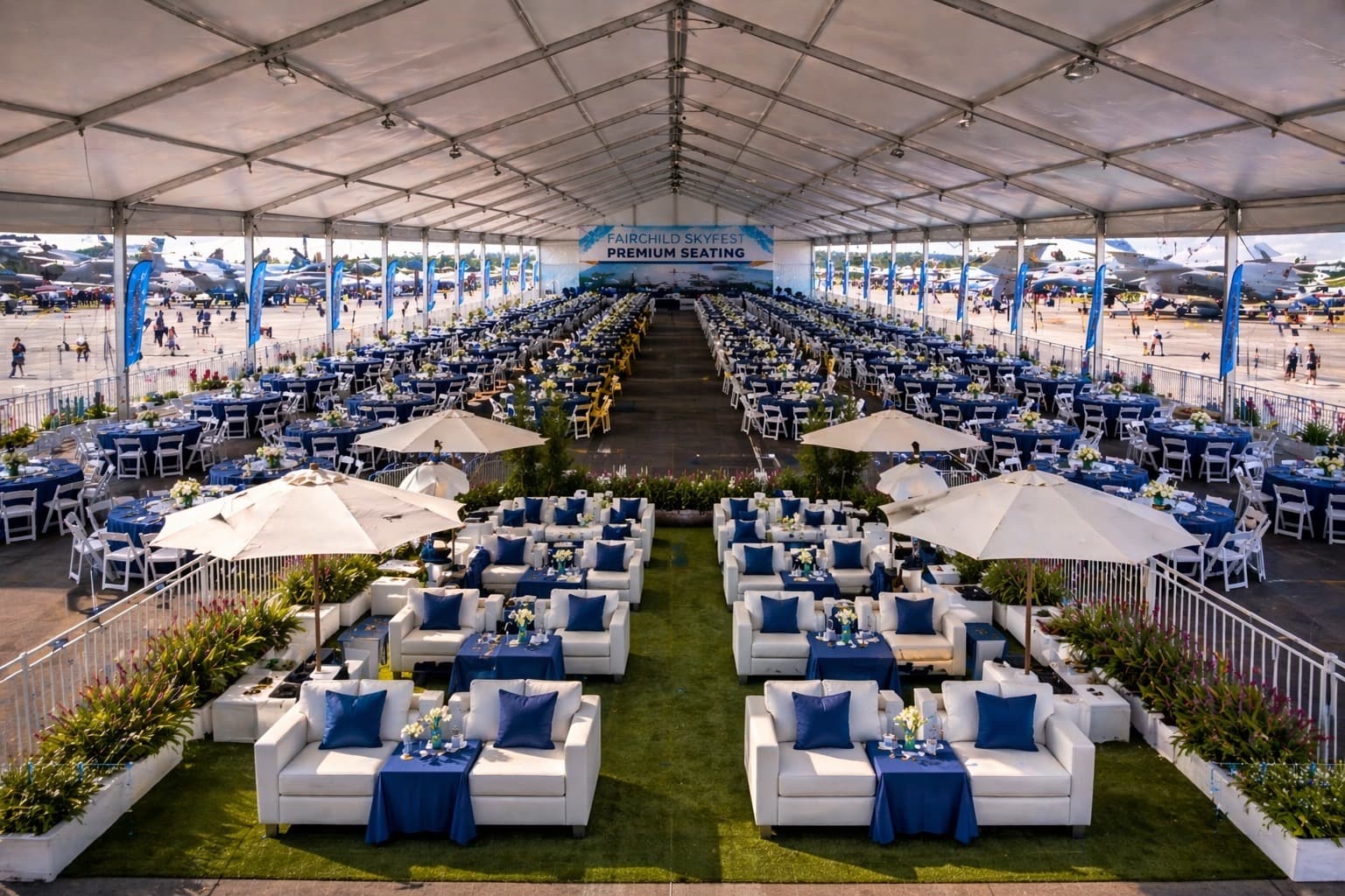 Admirals Club premium seating area with round dining tables, lounge sofas under umbrellas, white folding chairs, and a flight-line view of static-display aircraft
